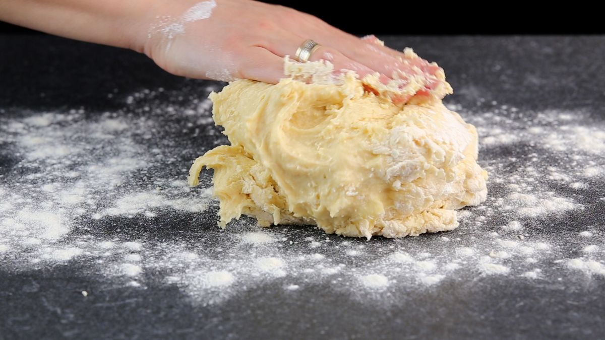 A hand touching a dough on a flour sprinkled table.