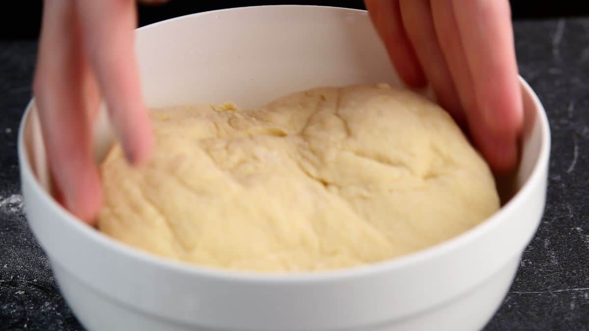 Hands putting a dough in a white bowl.