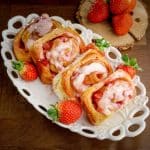Strawberries and cream sweet rolls on a white tray with ripe strawberries around.