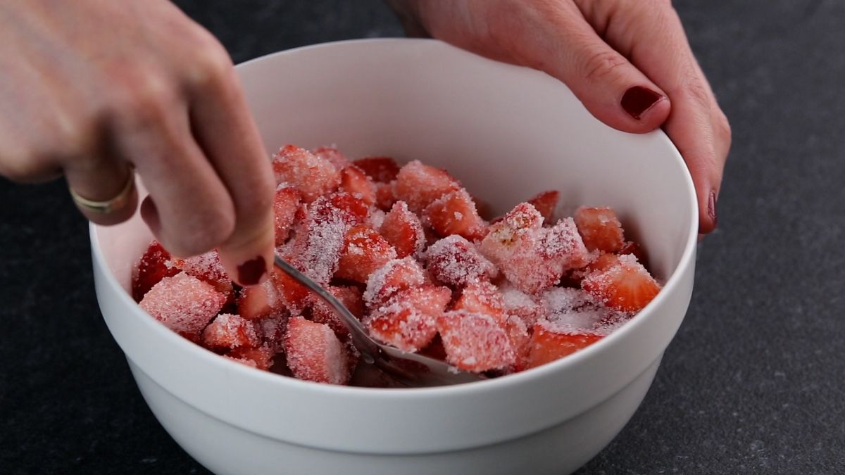 Hands mixxing sliced strawberries and sugar in a bowl.