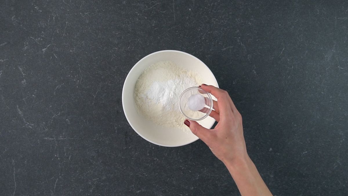 Hand holding a small bowl of ingredients over a big bowl.