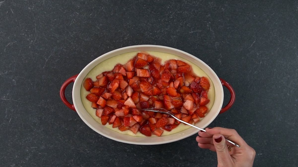 Hands spreading sliced strawberries in a caserolle.