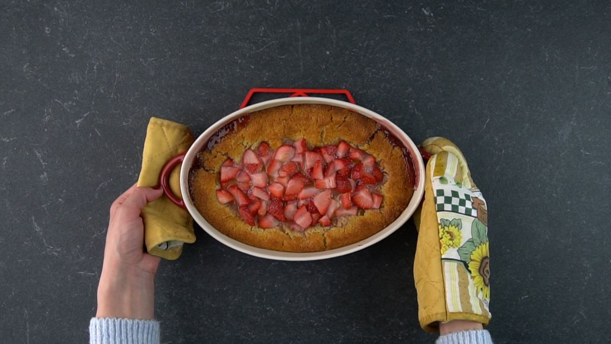 Hands holding freshly baked strawberry cobbler in a casserole.