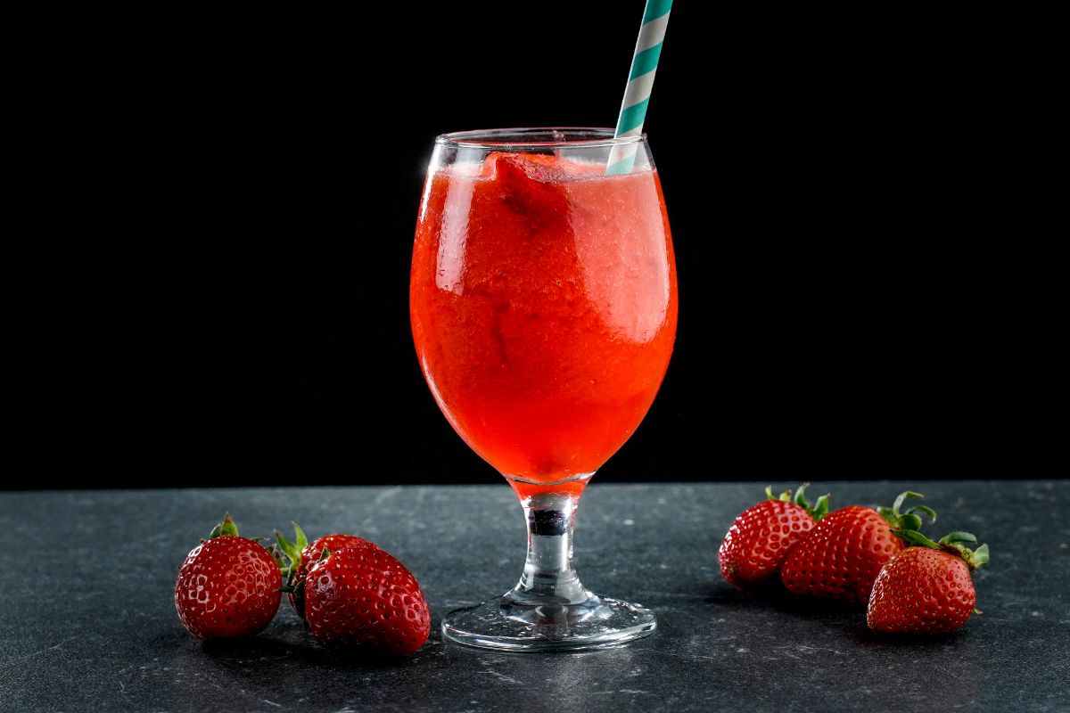 Strawberry daiquiri in a glass cup with a straw on the table with strawberries around.