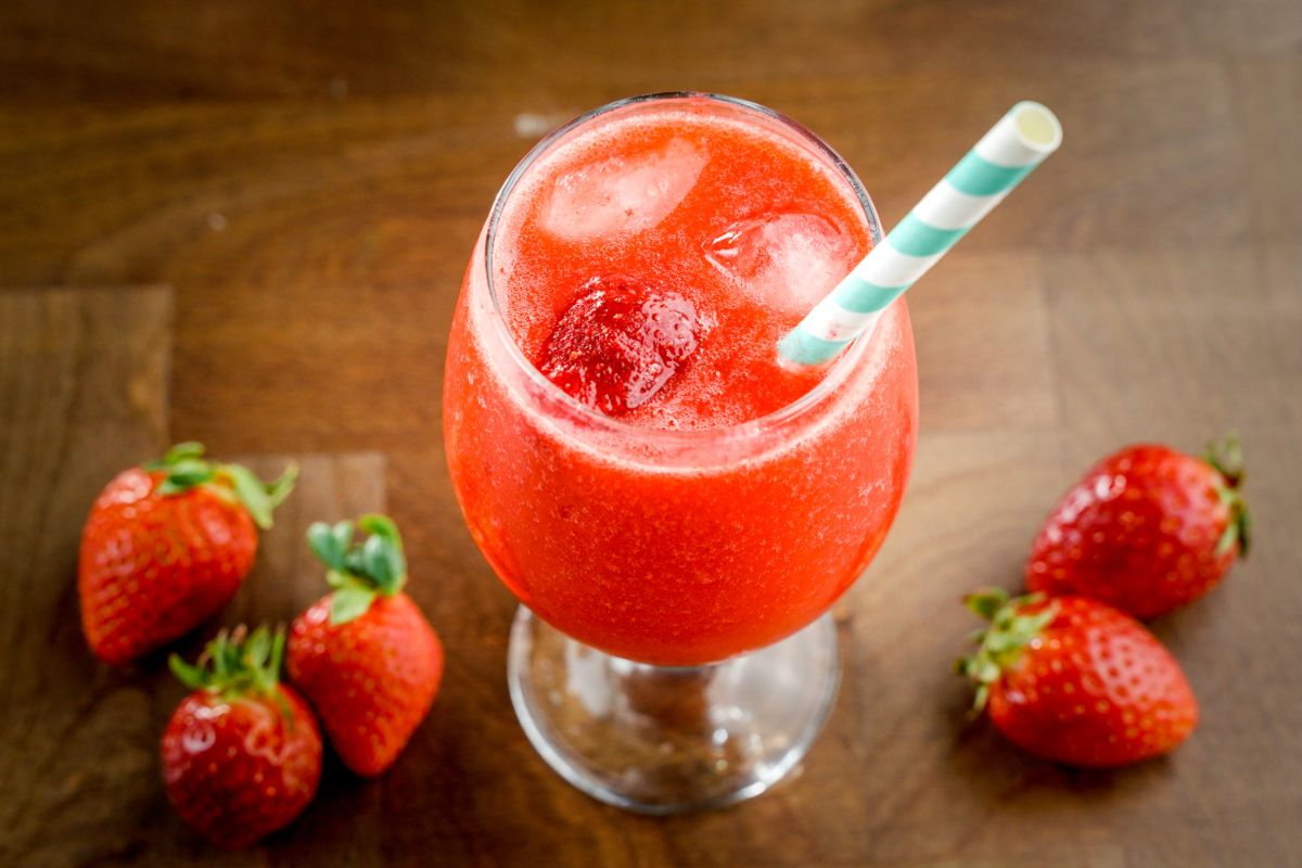 Strawberry daiquiri in glass cup with a straw and scattered strawberries around.