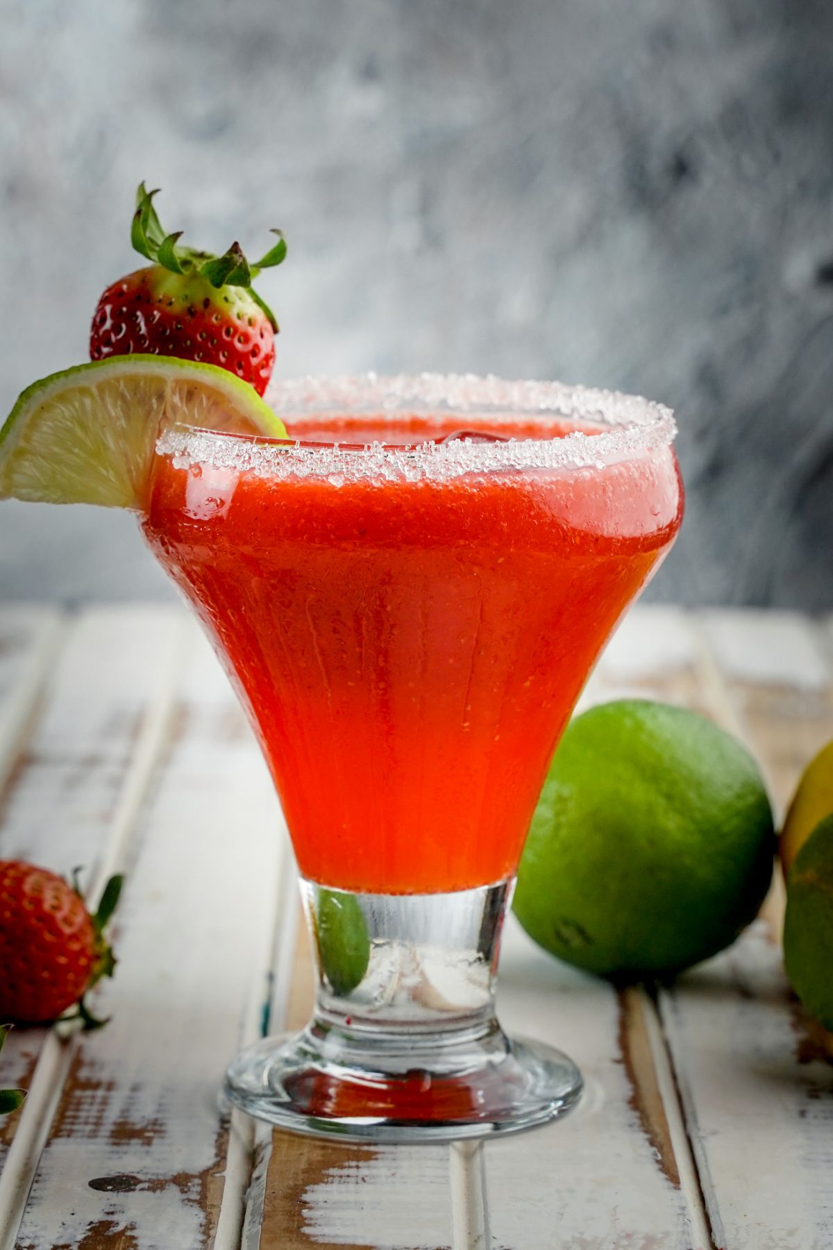 Strawberry daiquiri in a glass cup with lime strawberries.