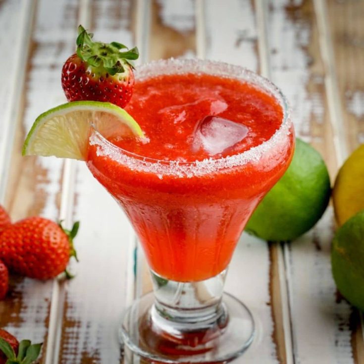 Strawberry daiquiri in a glass cup with slice of lime and strawberry.