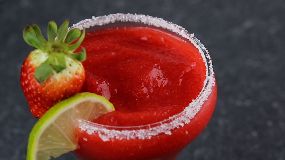 Strawberry daiquiri ina glass cup with  a lime and a strawberry.