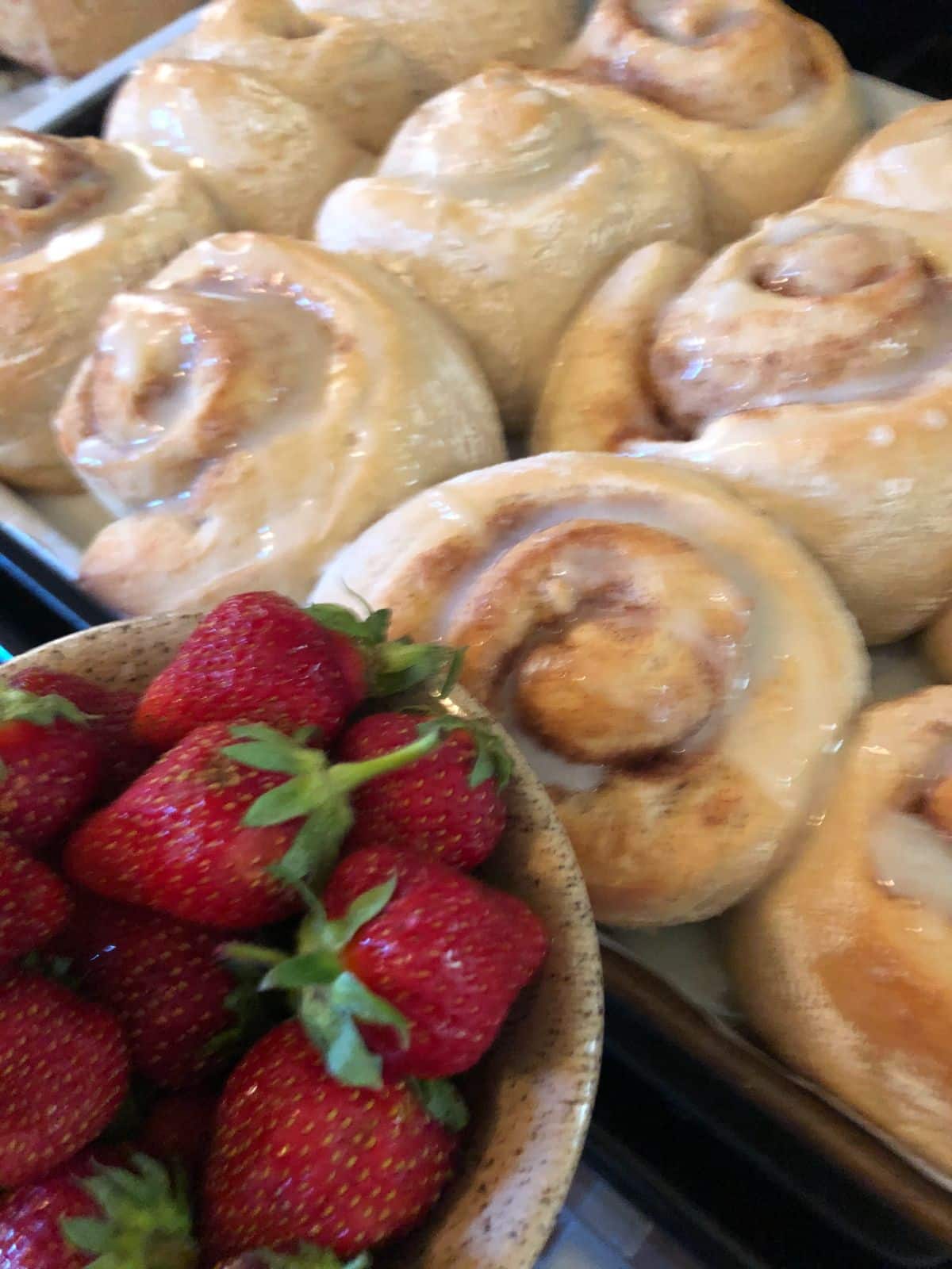 A bowl of fresh strawberries for eating next to homemade cinnamon rolls