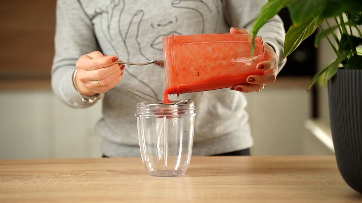 Woman puring blended strawberries from blender into container.