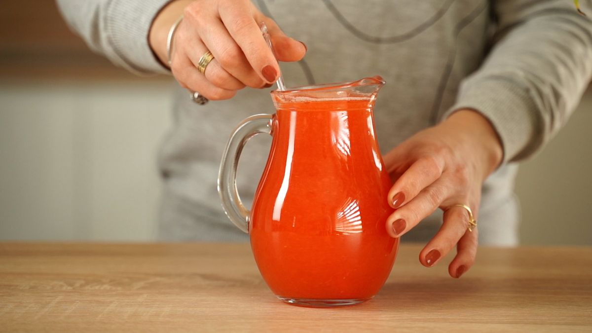 Woman stirring a strawberry lemonade in a glass pitcher.