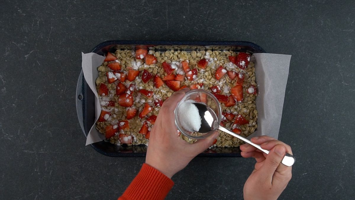 Hands pouring with spoon a sugard over mixture in a baking tray.