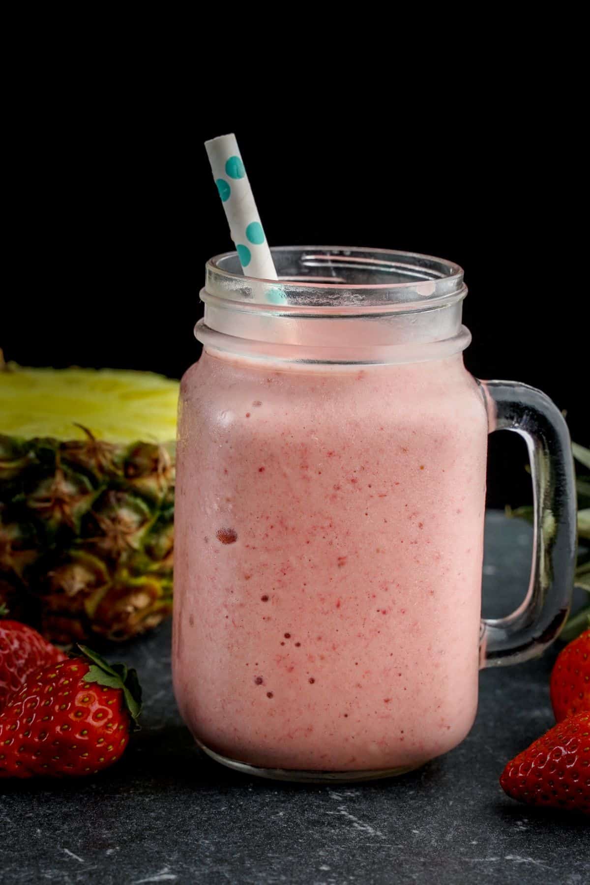 A close-up of a glass jar of Strawberry Pineapple Smoothie with a straw.