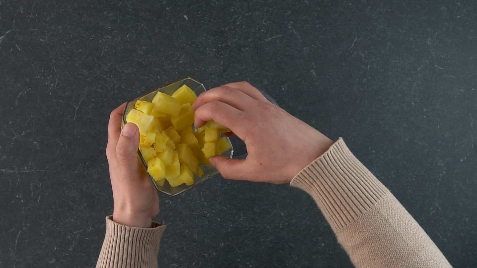 Hands holding and adding a sliced pineapple in a blender.