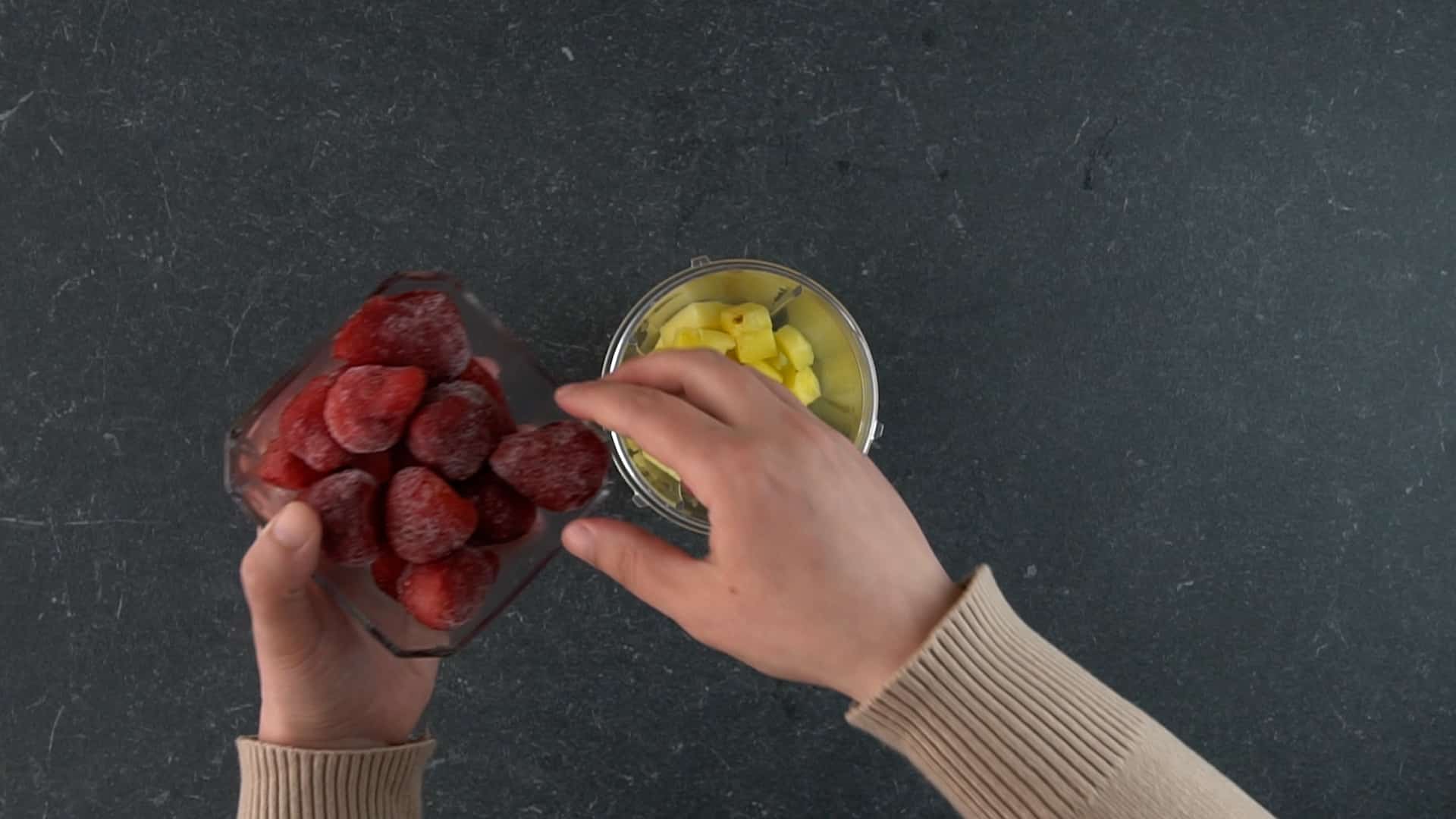 Hands holding a bowl of strawberries over a blender.