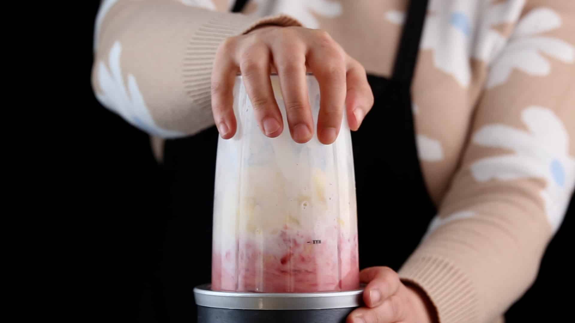 Hands holding a blender with a smoothie mixture.
