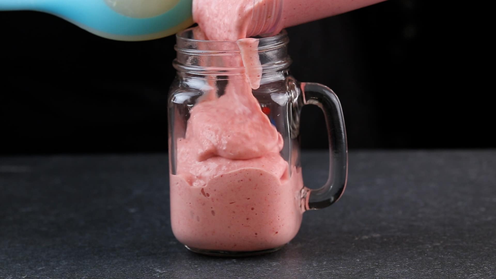 A close-up of pouring a smoothie in a glass jar.