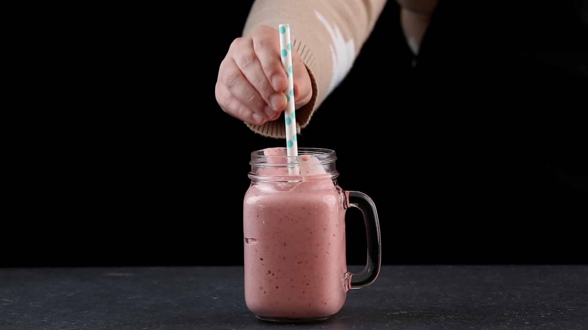 A hand adding a straw in a glass jar of smoothie.