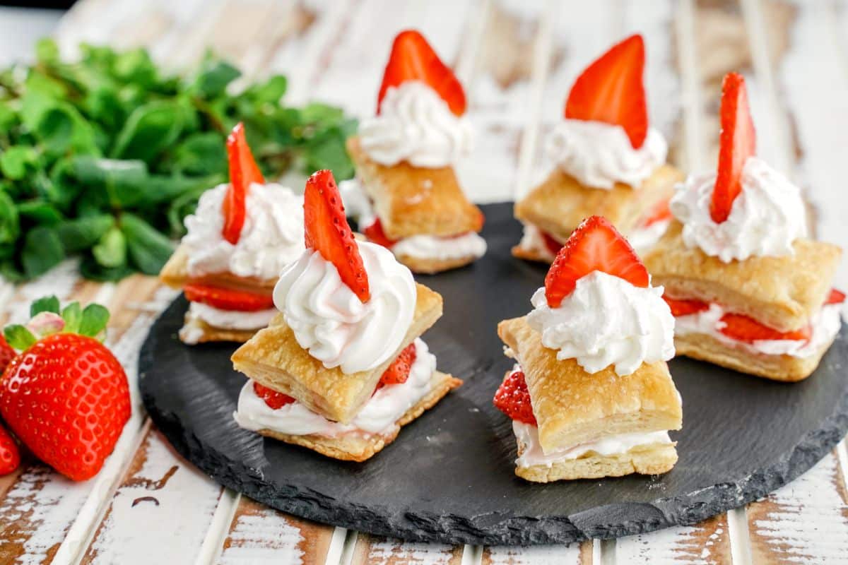 Six strawberry shortcake puffs on a black tray on a wooden table.