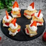 Six strawberry shortcake puffs on a black tray.