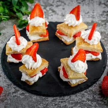Six strawberry shortcake puffs on a black tray.