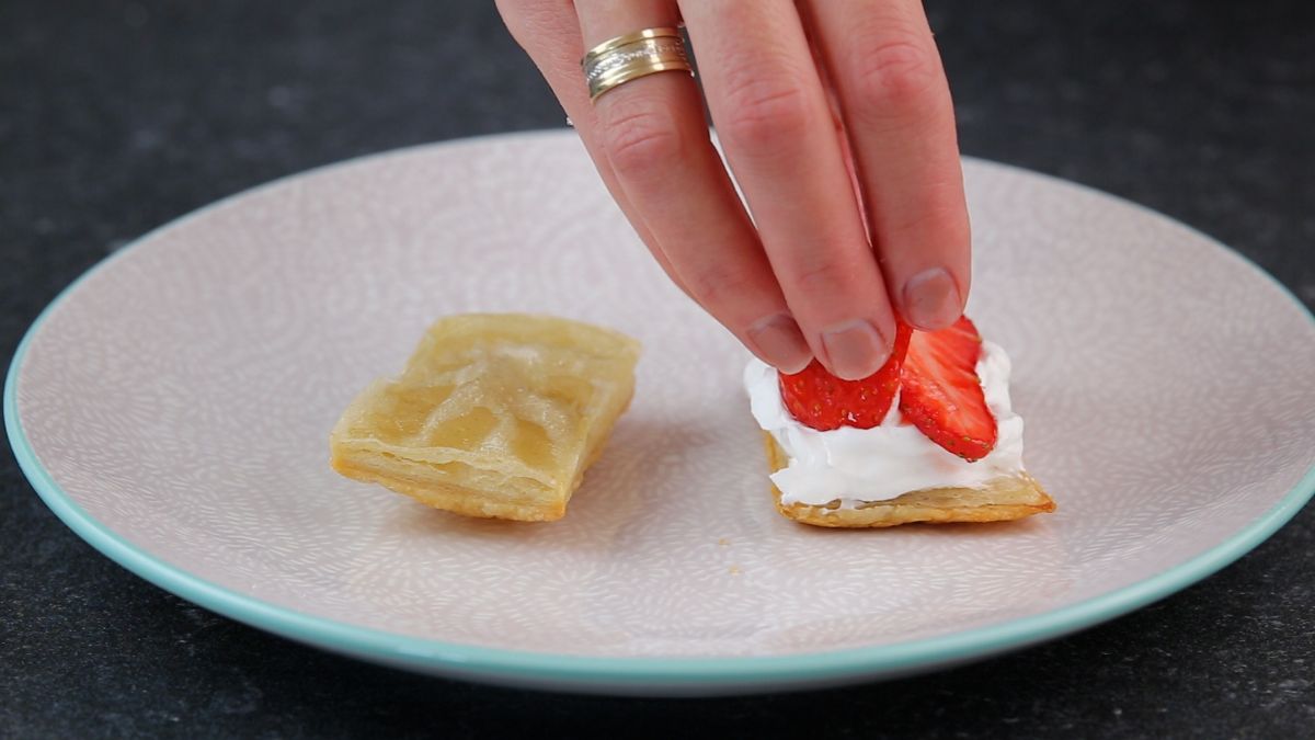 A hand putting sliced strawberries on a top of a strawberry shortcake puff.
