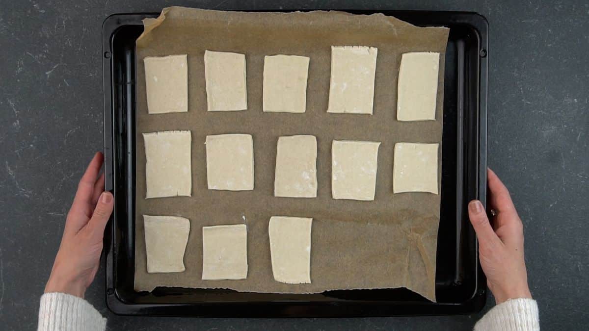Hands holding a cooking tray with a parchment paper and pieces of dough.