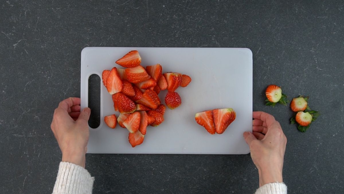 Hand touching a cutting board with slcied strawberries.