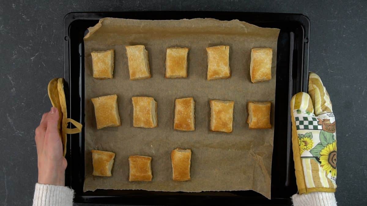 Hands holding a baking tray with a parchment paper with baked doug pieces.