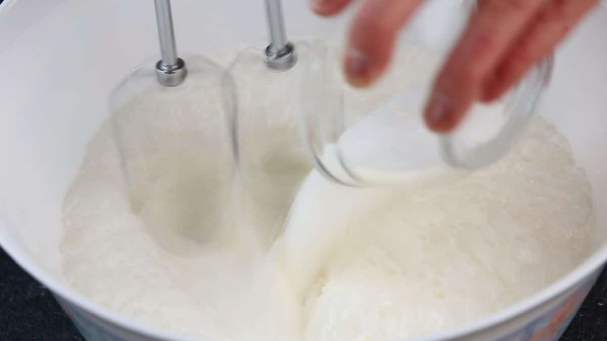 A close-up of puring sugar in a white bowl of a whipped cream.