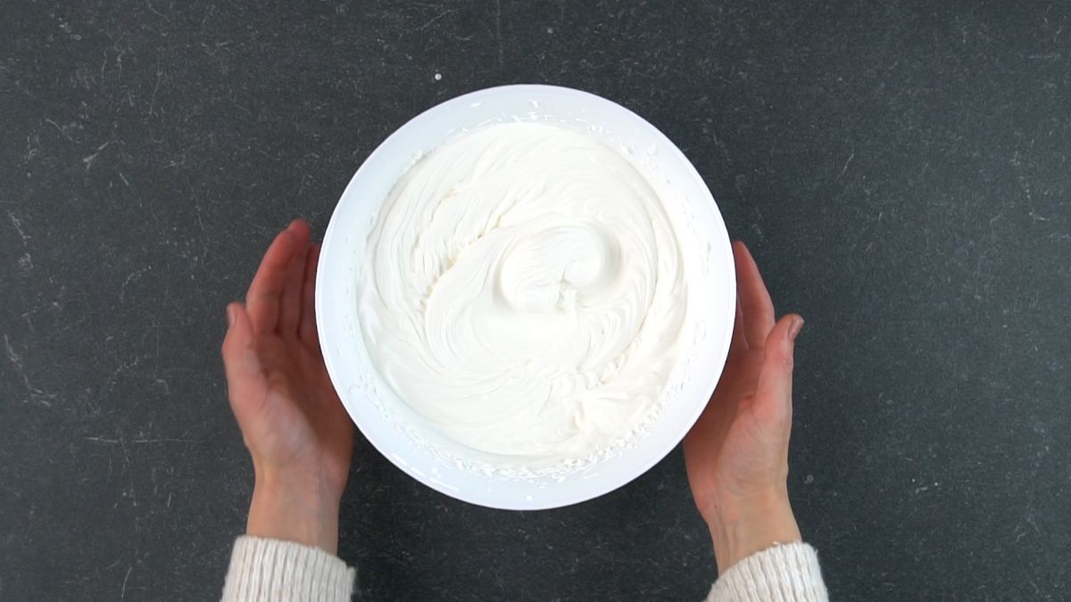 Hands holding a white bowl full of a whipped cream.