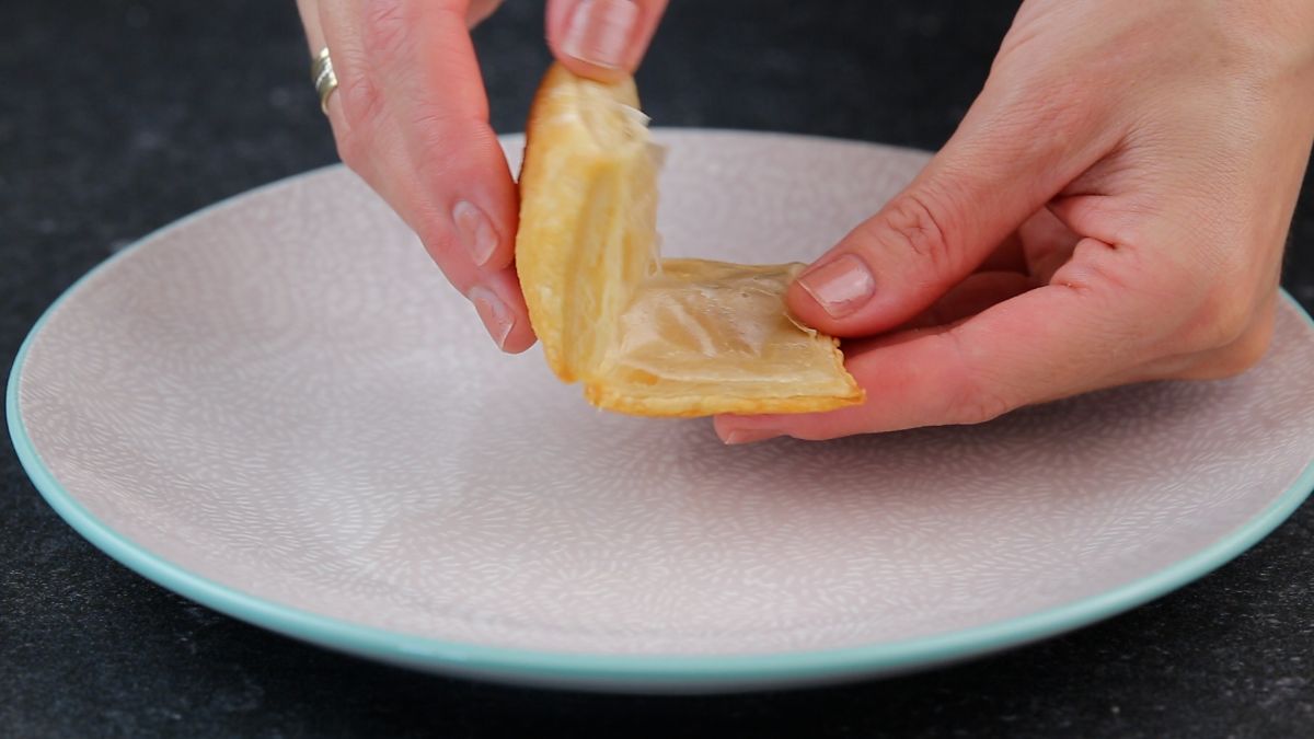 Hands holding a baked dough piece over a plate.