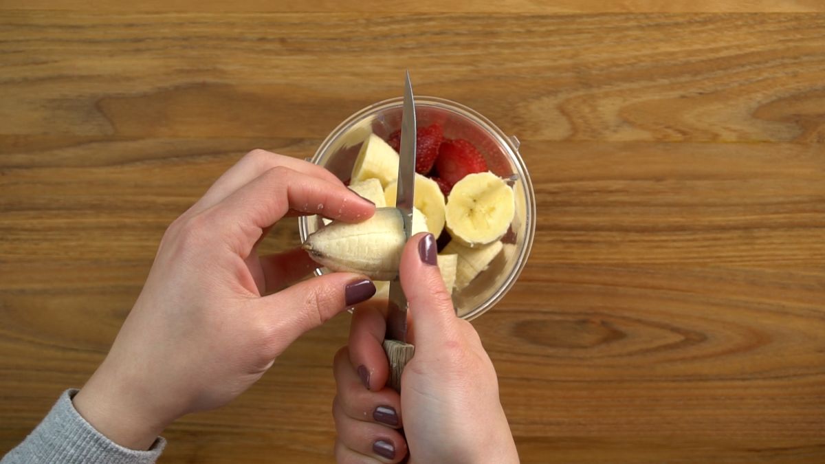 Hands cutting a banana with knife over blender.