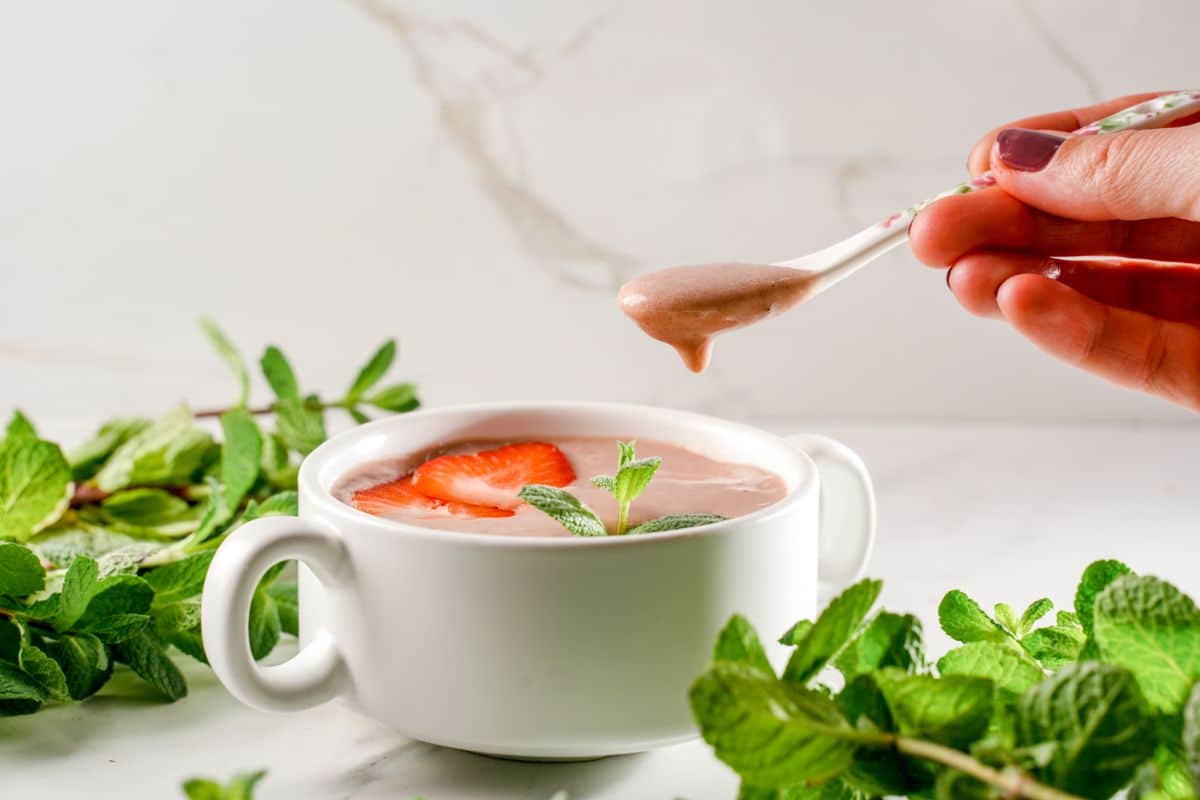 Hand holding spoon over a strawberry vanilla smoothie bowl.