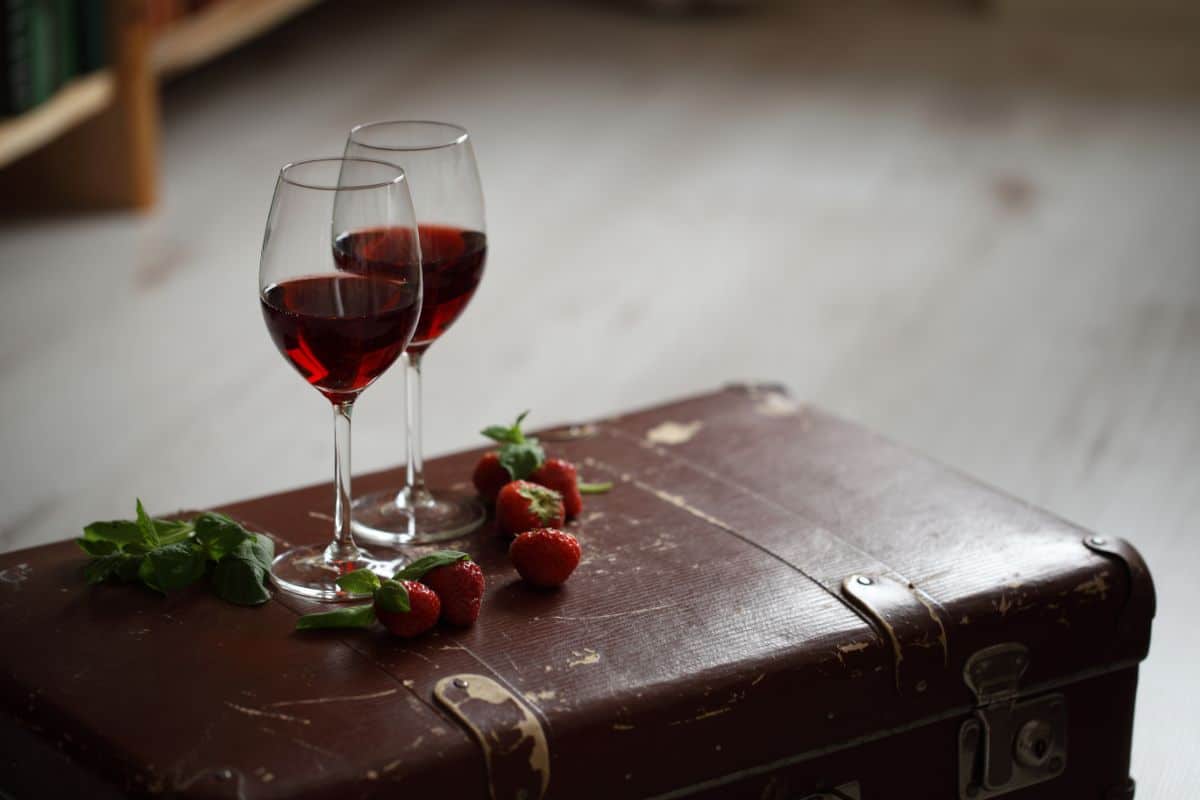 Two glasses full of wine on leather box near strawberries and mint