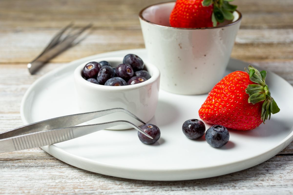 Tweezers, blueberrie and strawberries on the white plate.