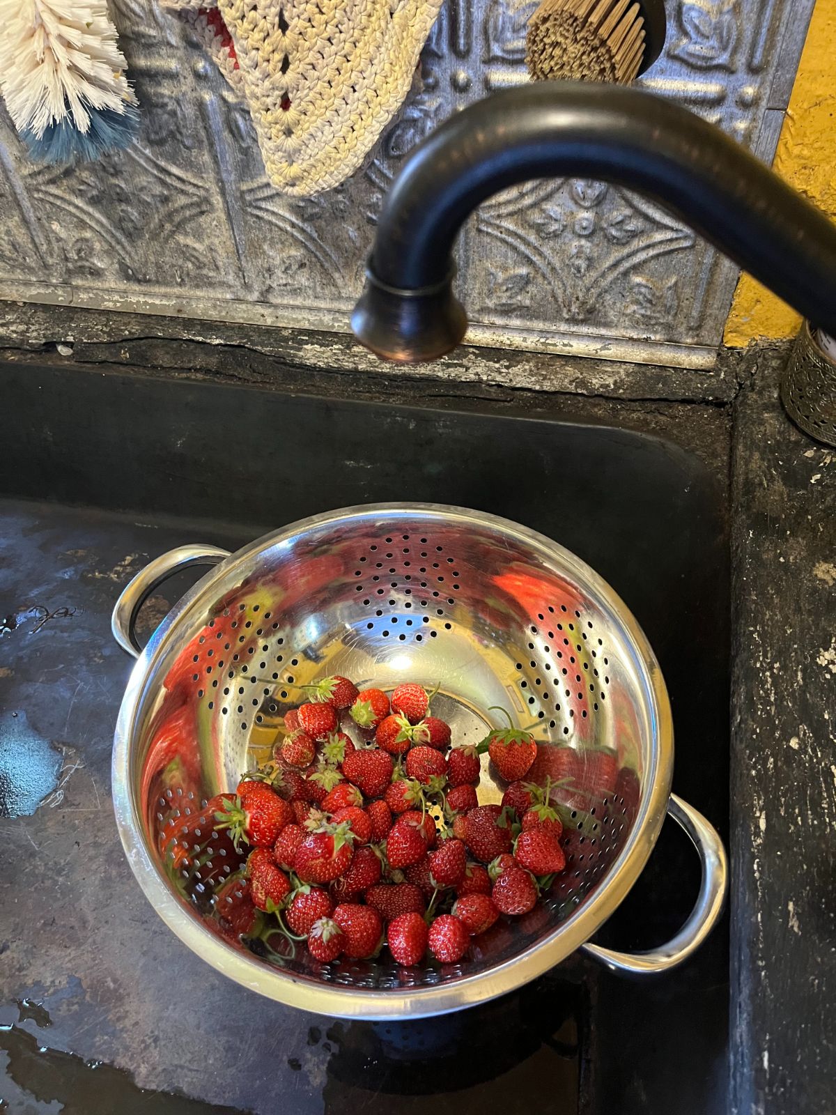 A colander of strawberries in a sink being washed