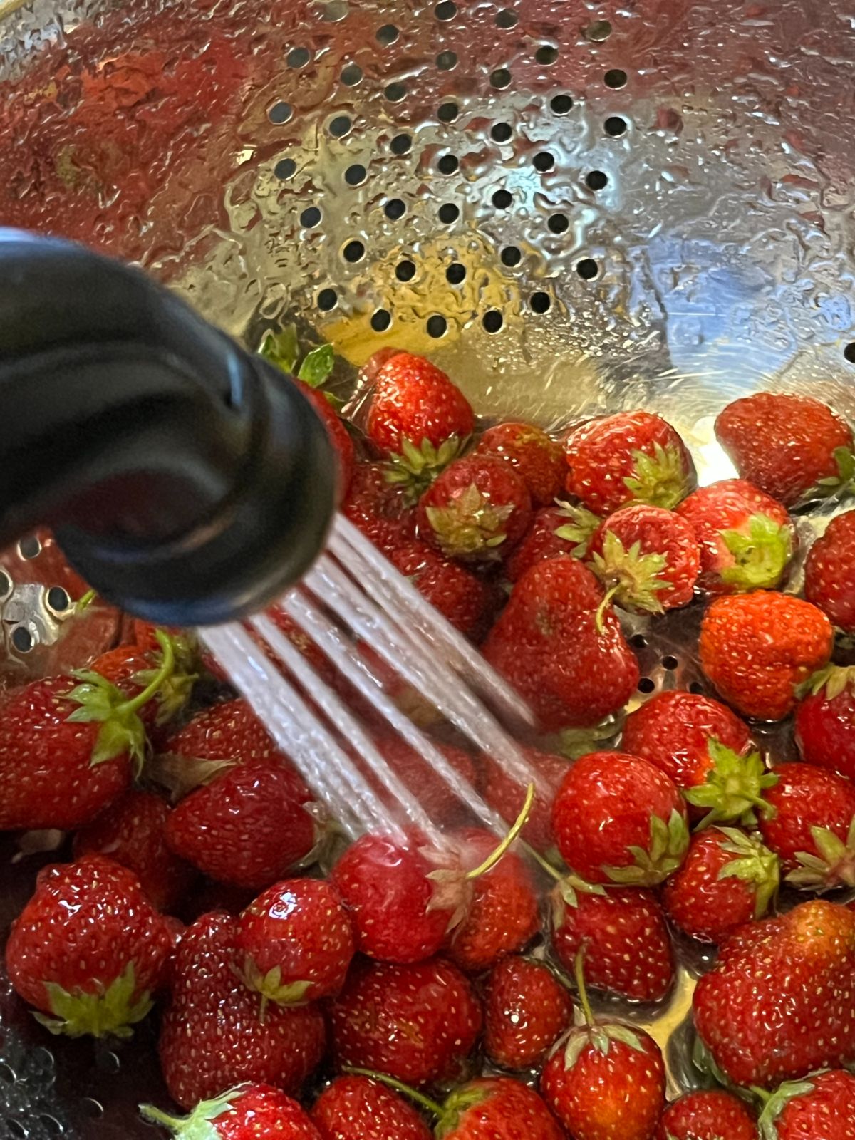 Strawberries being washed with a kitchen sprayer