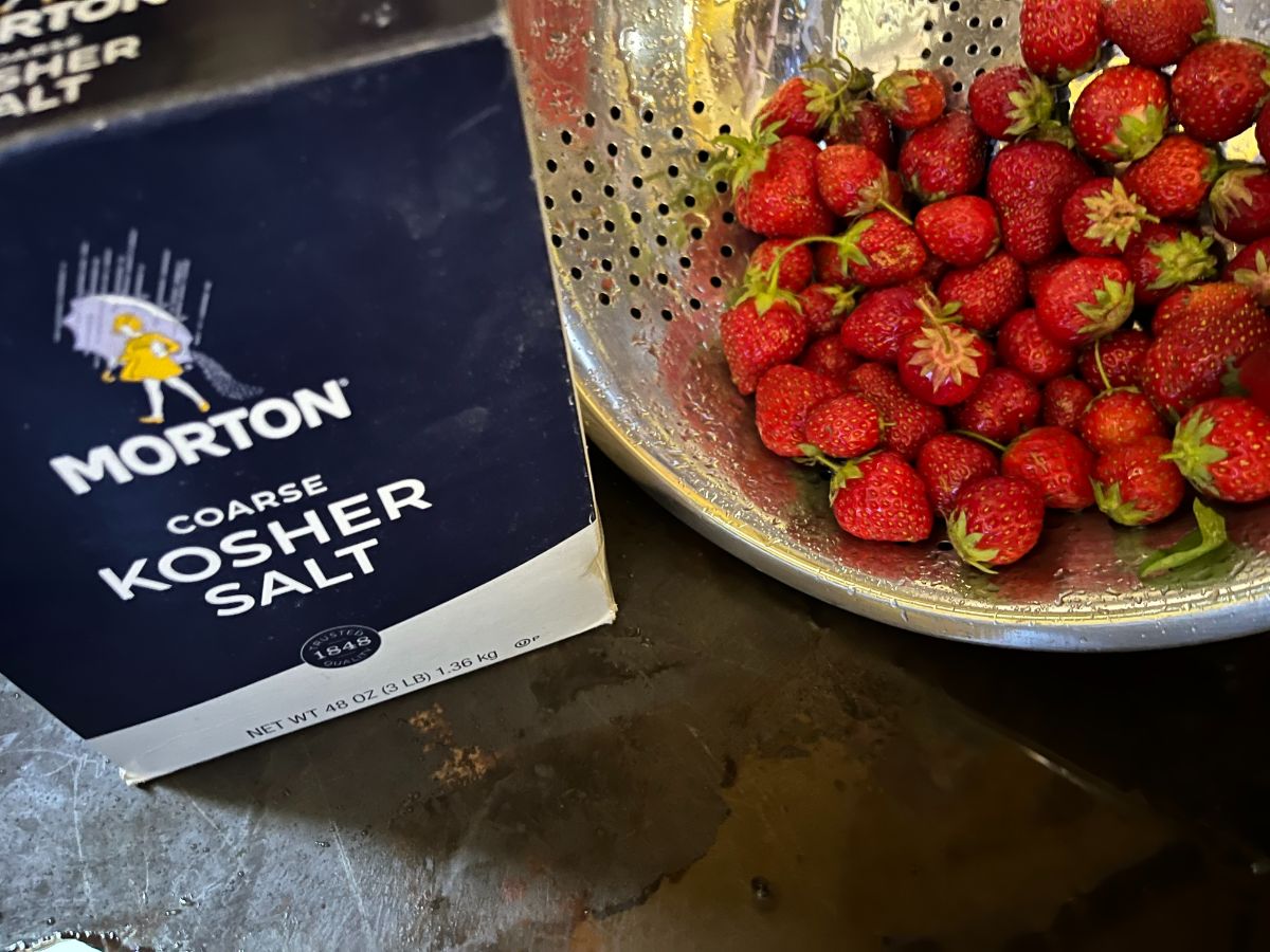 A colander of strawberries next to a box of salt